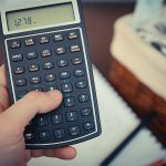 A close-up of a hand holding a calculator with financial calculations.